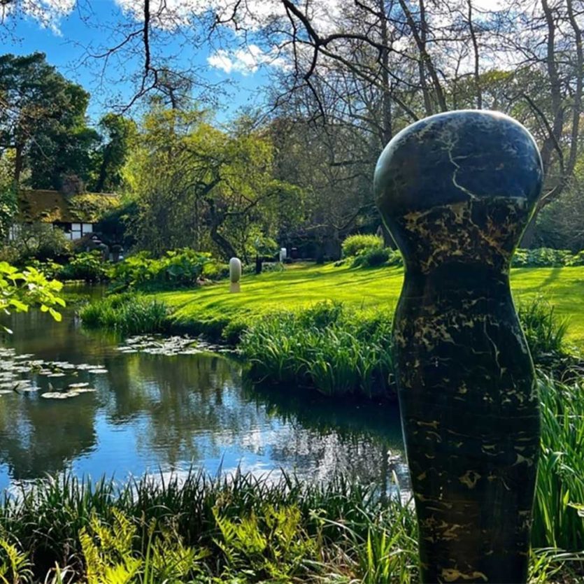 a lakeside view of the Hannah Peschar Sculpture Garden